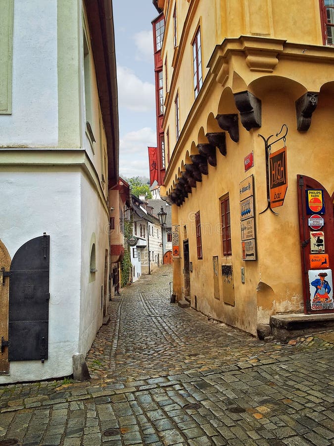 Cesky Krumlov, Czech Republic-October 1, 2014: Narrow Masna Street bends turn right after the 3-floor yellow medieval houses hosting pubs and souvenir shops on the right and grey plaster facade of another building on the left. Cesky Krumlov, Czech Republic-October 1, 2014: Narrow Masna Street bends turn right after the 3-floor yellow medieval houses hosting pubs and souvenir shops on the right and grey plaster facade of another building on the left.